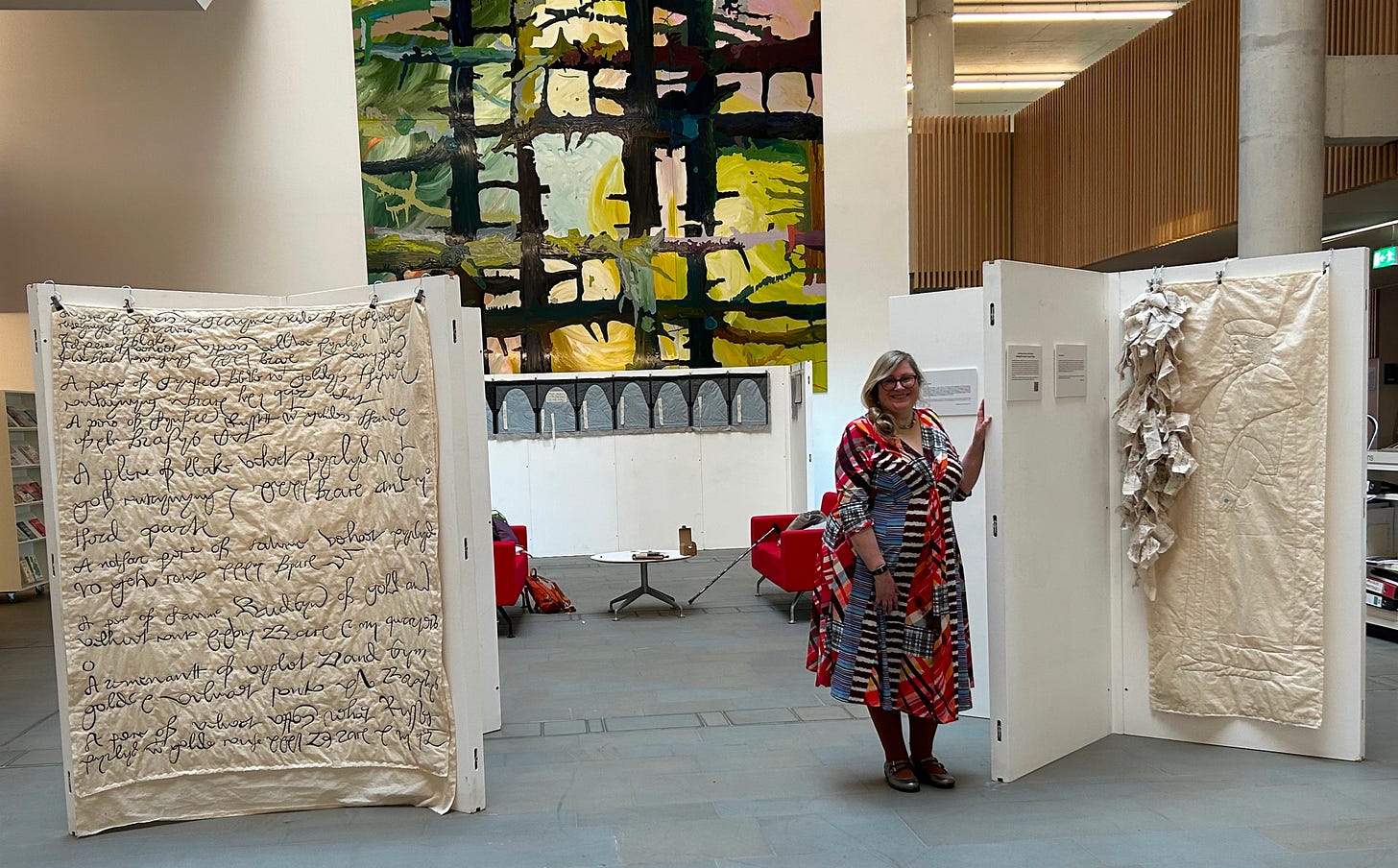 A woman in a colourful dress standing between exhibition display stands showing textile work. 