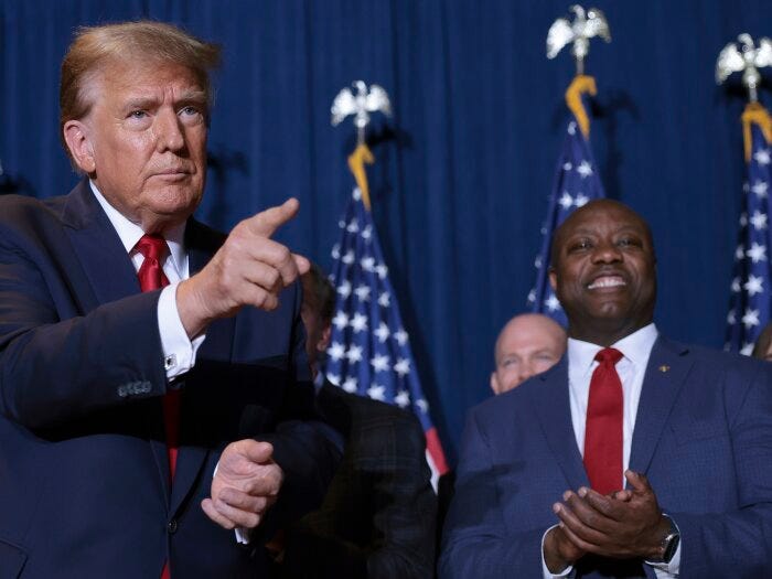 Republican presidential candidate and former President Donald Trump gestures to supporters as Sen. Tim Scott (R-SC) looks on during an election night watch party at the State Fairgrounds on February 24 in Columbia, S.C.