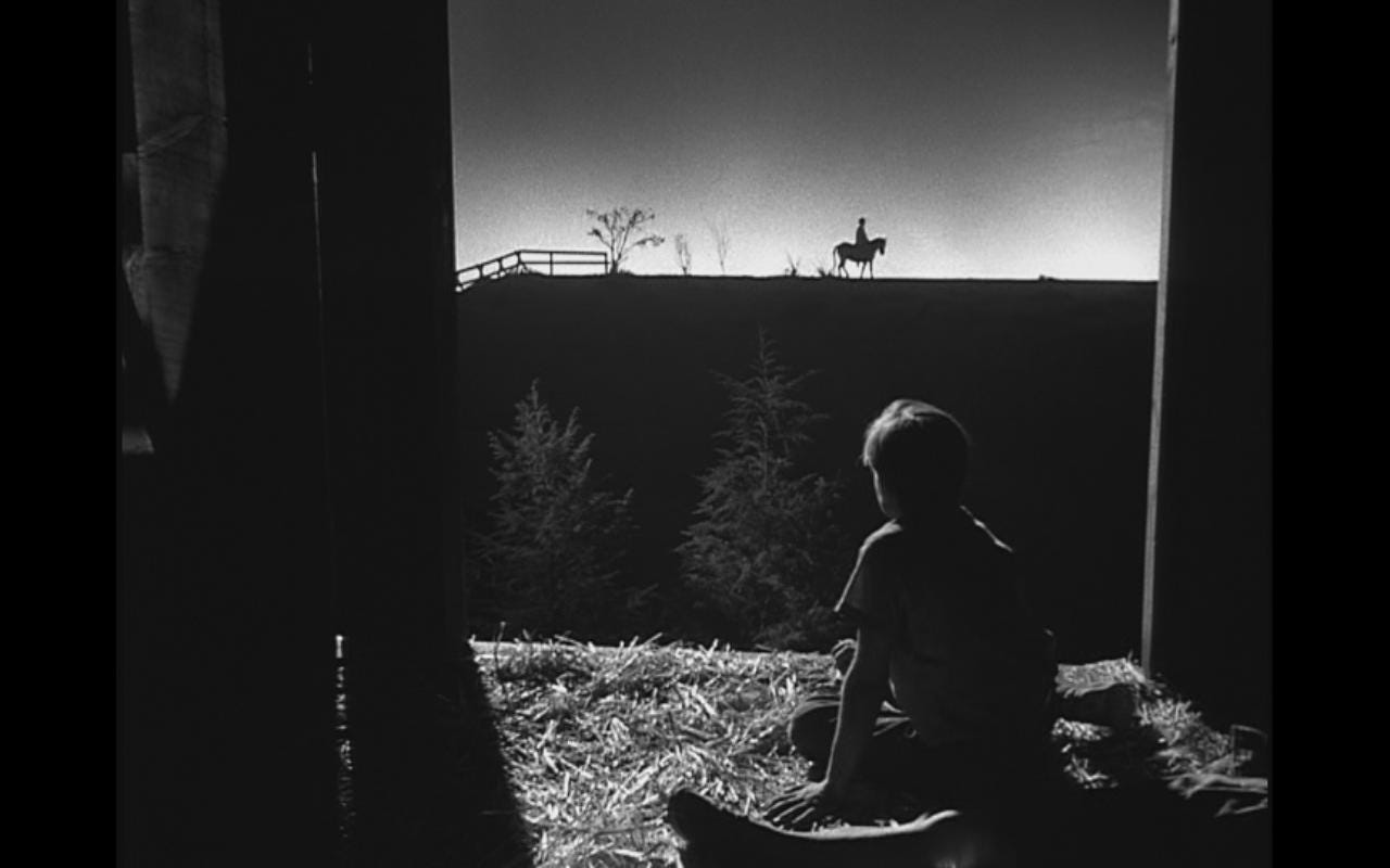 A child watches a man on a horse on the horizon from a bale of hay in a barn in "The Night of the Hunter" (1955)