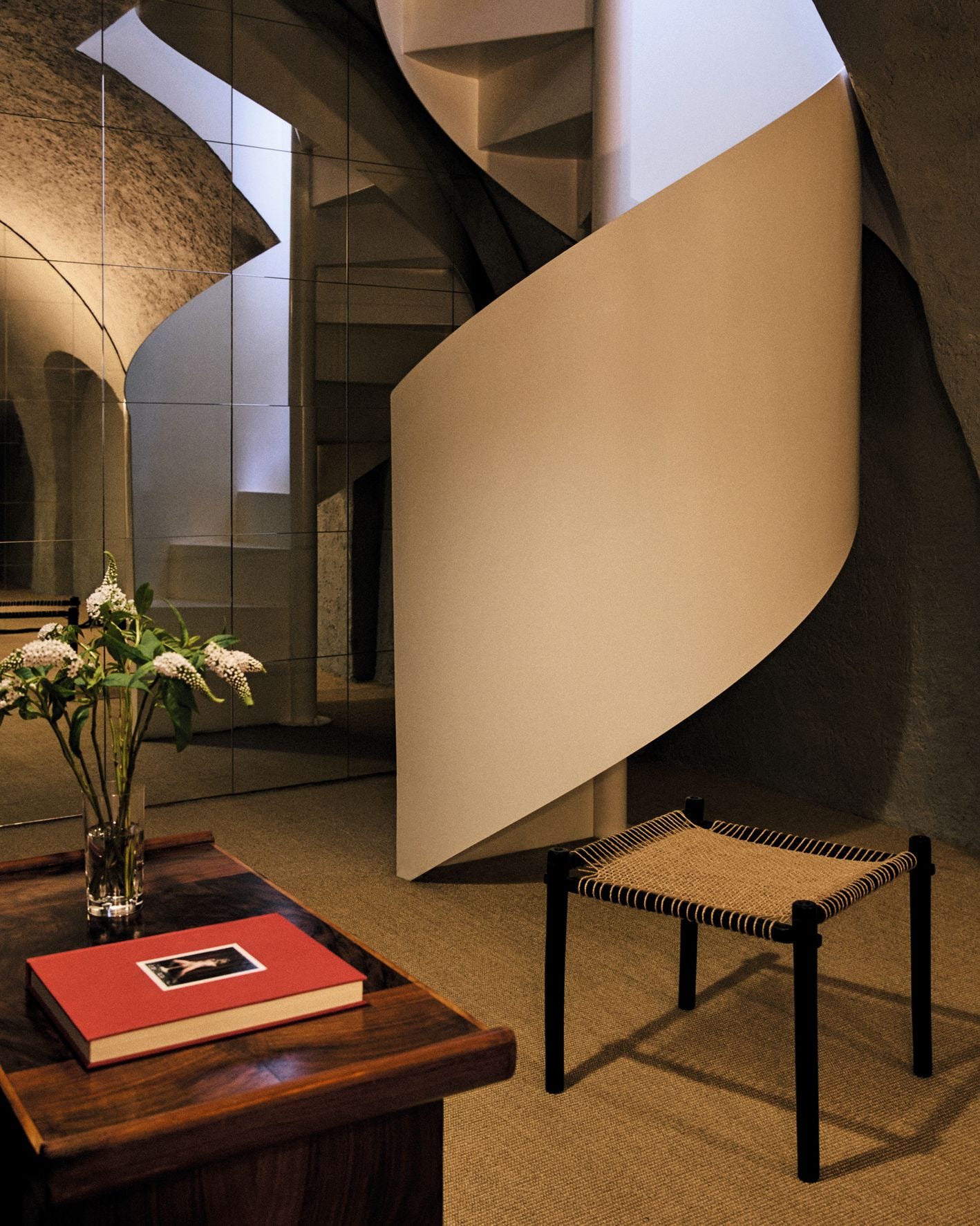 Scala a chiocciola bianca parete specchiata tavolino in legno vaso con fiori sgabello in corda e legno