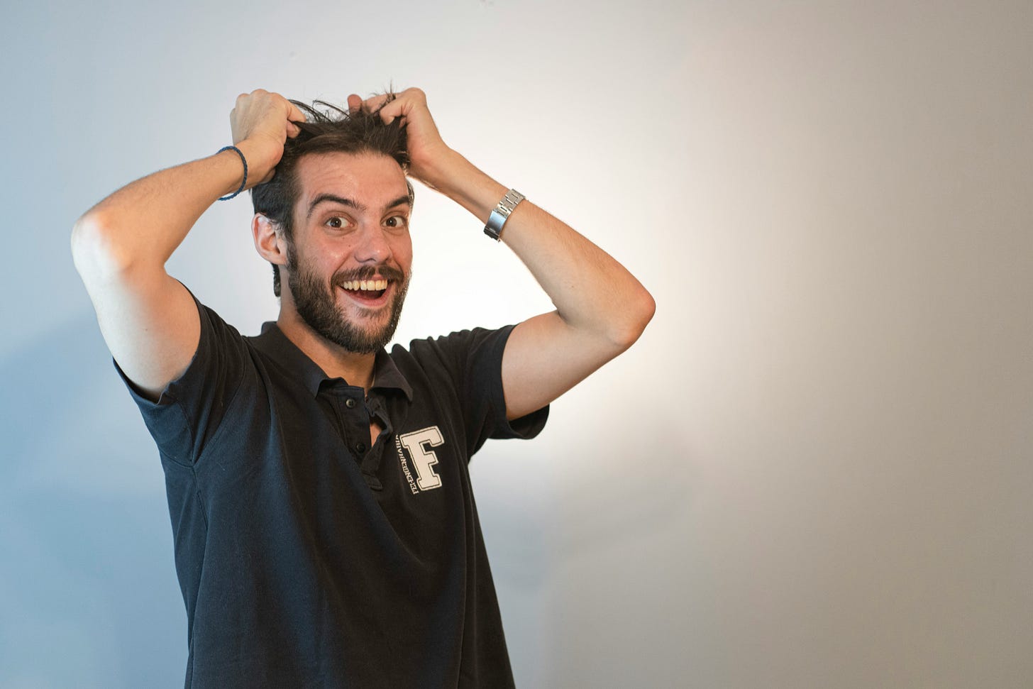 Excited man with beard pulling hair in surprise gesture wearing black polo shirt with F logo Excited man with beard pulling hair in surprise gesture wearing black polo shirt with F logo
