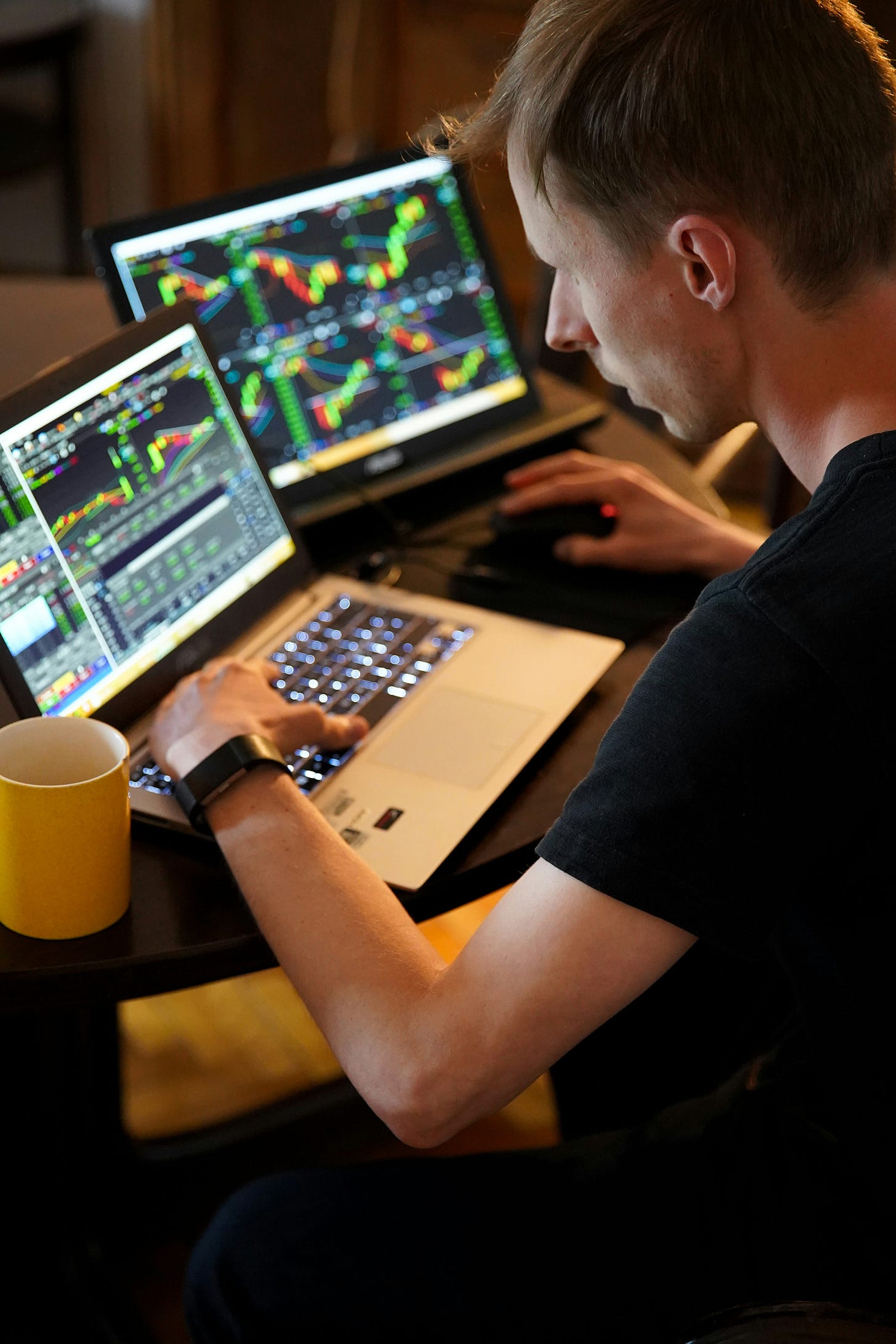 Person analyzing financial data and trading charts on dual computer monitors with colorful market indicators and price movements