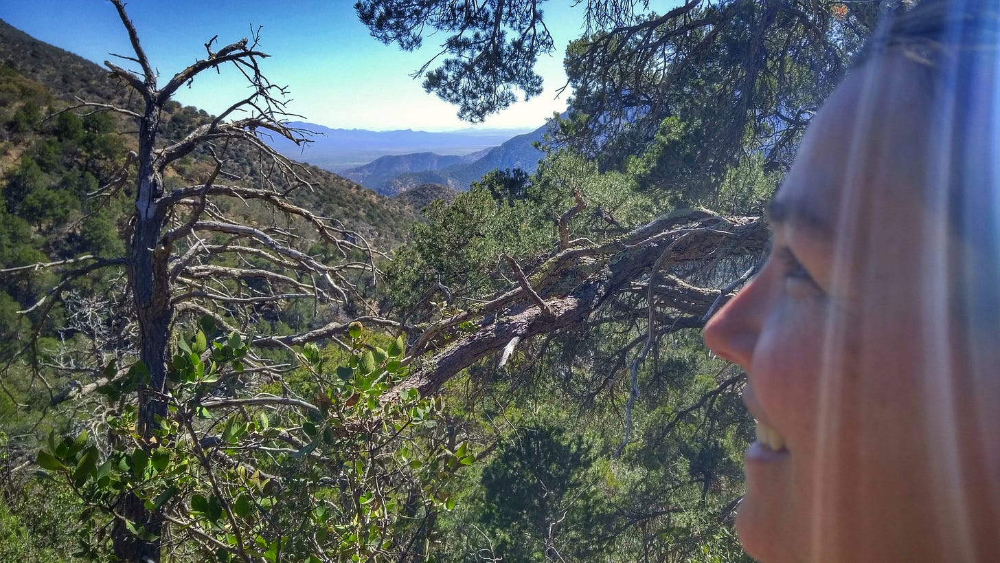 woman looking over a mountain valley with sun beams coming down over her smiling face