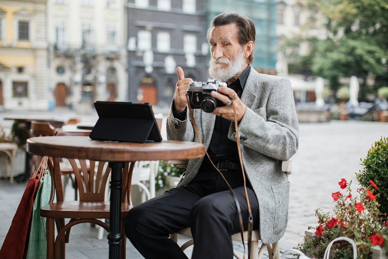 confident-senior-man-sitting-at-cafe-terrace-and-using-digital-tablet-with-retro-camera-bearded-pensioner-reviewing-pictures-and-showing-thumb — Getty Images with permission from Unsplash+ confident-senior-man-sitting-at-cafe-terrace-and-using-digital-tablet-with-retro-camera-bearded-pensioner-reviewing-pictures-and-showing-thumb — Getty Images with permission from Unsplash+