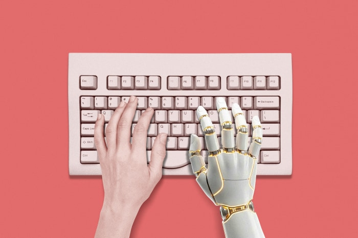 A human hand and a robot hand on a computer keyboard, symbolizing AI and human intelligence.