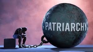 A man shackled to a huge iron ball on which the word 'Patriarchy' is written. A man shackled to a huge iron ball on which the word 'Patriarchy' is written.