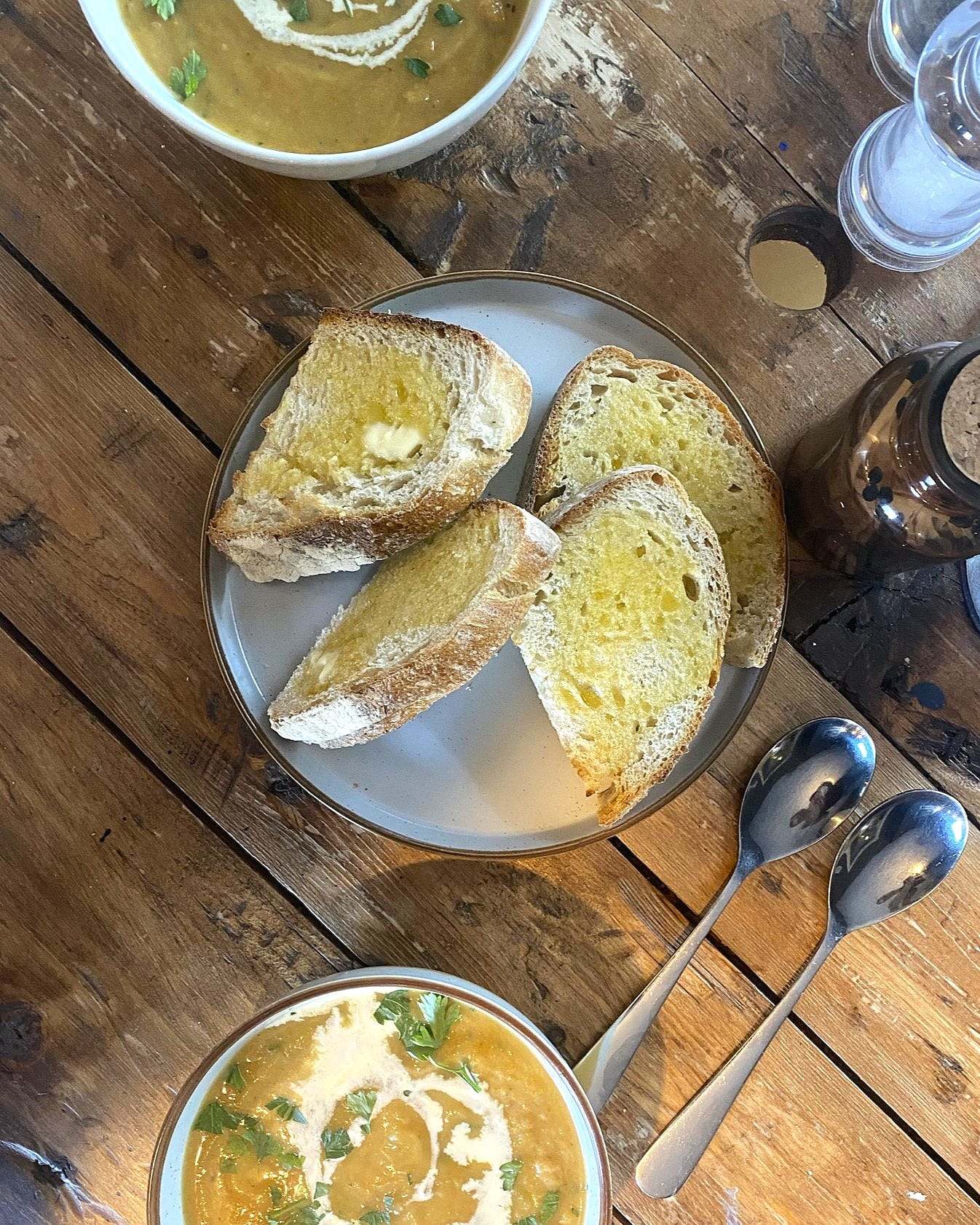 Image shows a table set with a plate of buttered bread and two bowls of soup