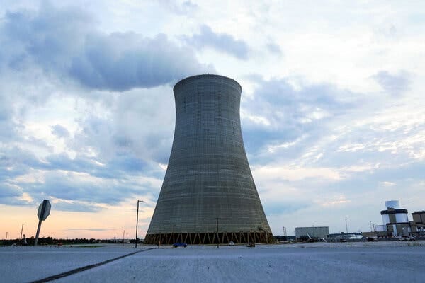 A single, gray power-plant cooling tower stands against a cloudy blue-gray sky.