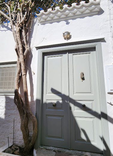 Collage of three images from Hydra, Greece: a plaque mounted on stone dedicating a park bench to Leonard Cohen, a close-up of the plaque with bilingual text in English and Greek, and a pale green front door believed to be Cohen’s home, framed by whitewashed walls and a tree.