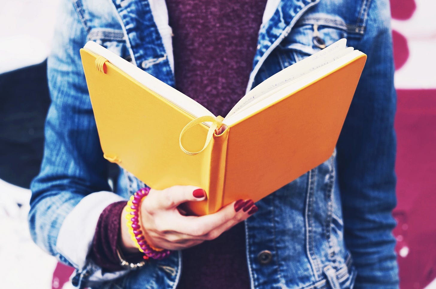 close-up of woman's torso wearing denim jacket reading from a yellow noteook