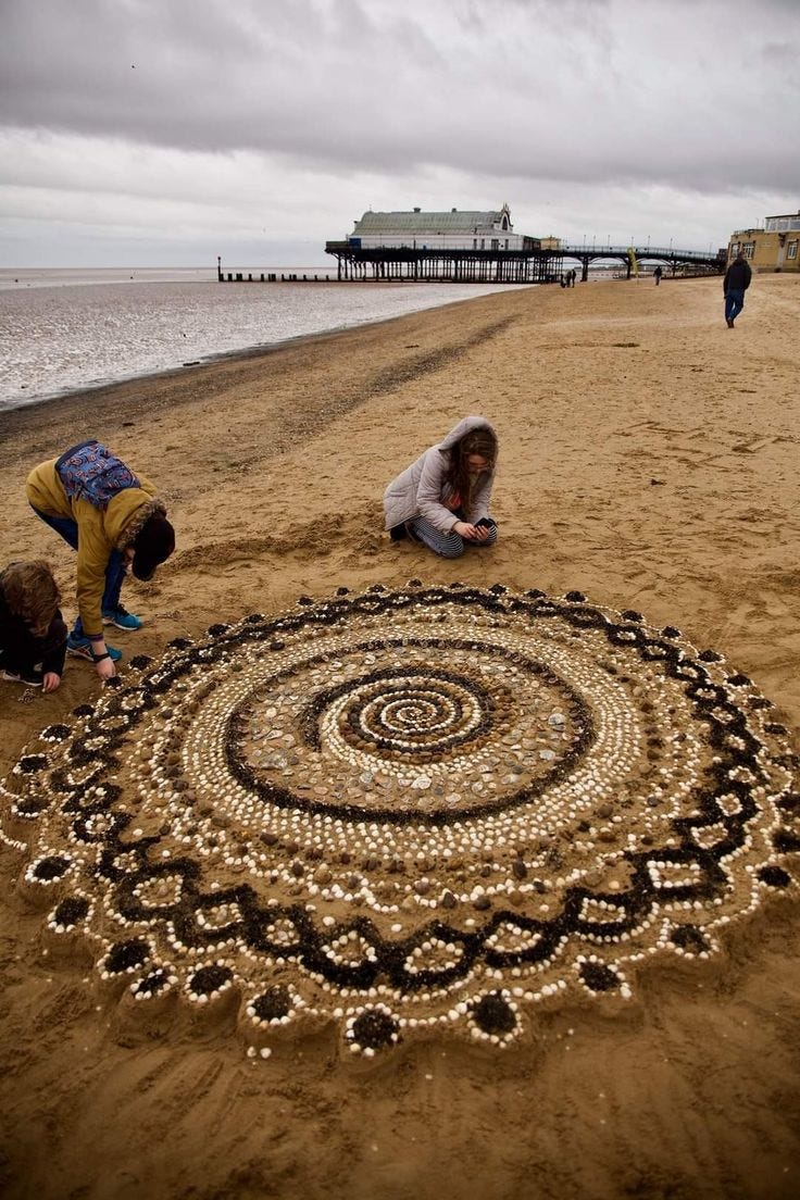 This may contain: two people kneeling down on the beach next to a circular artwork