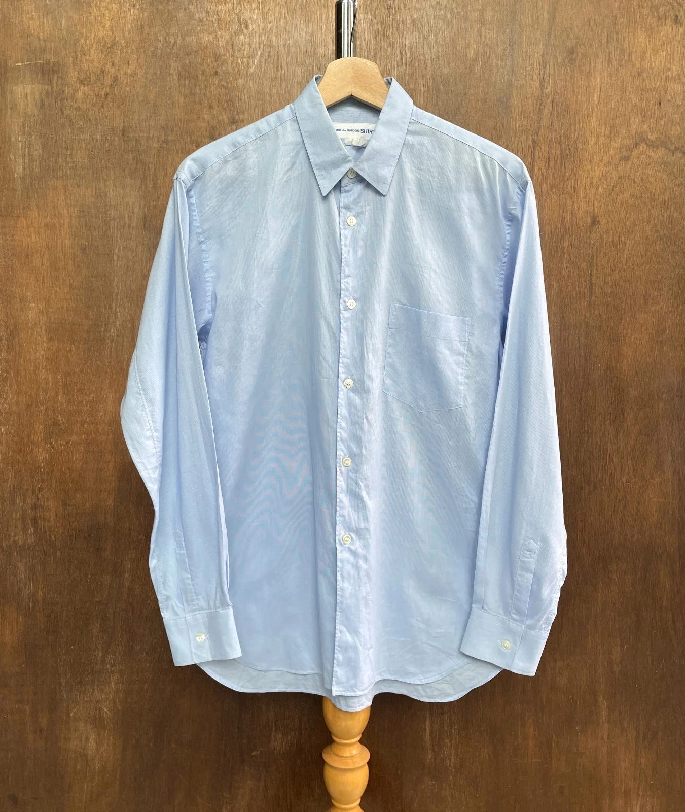 Light blue COMME des GARCONS shirt with textured pattern, button-down collar, and “Made in France” label on hem. Light blue COMME des GARCONS shirt with textured pattern, button-down collar, and “Made in France” label on hem.