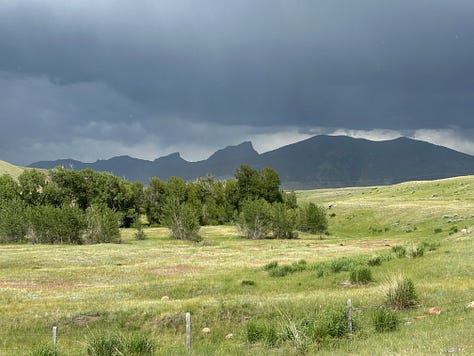 Mountain range surrounded by storm clouds and sun and grassy fields