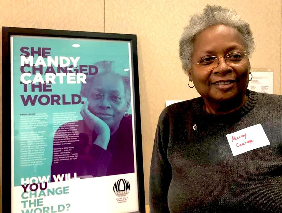 Mandy standing next to a poster from National Organization of Women (NOW) with her photo and the caption "Mandy Carter - She changed the world. How will you change the world?"