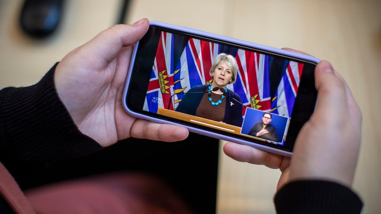 A person watches a news conference with B.C. provincial health officer Dr. Bonnie Henry in Feb. 2021.