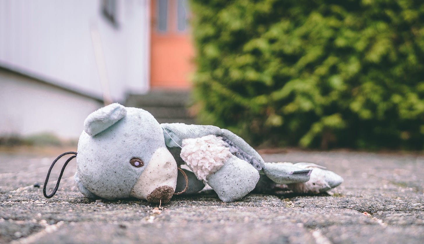 A ragged, light blue teddy bear is ripped on the ground.