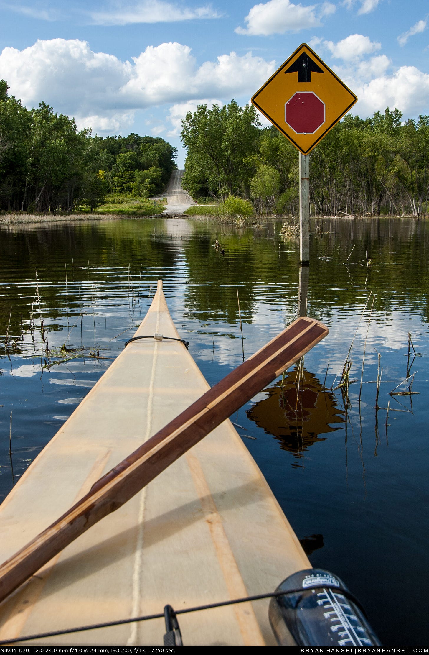A skin-on-frame kayak at a stop sign in a flooded area. There's a road leading out of the water.
