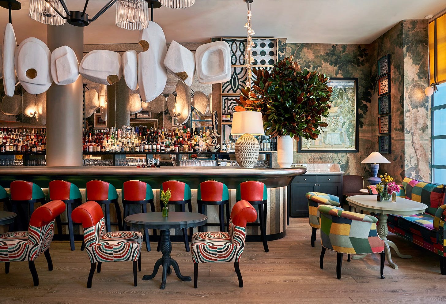 The bar at Warren Stree Hotel in Tribeca. Red and teal leather bar stools stand at a pewter-topped bar. Overhead hangs an abstract sculpture in white and gold that runs the length of the bar.