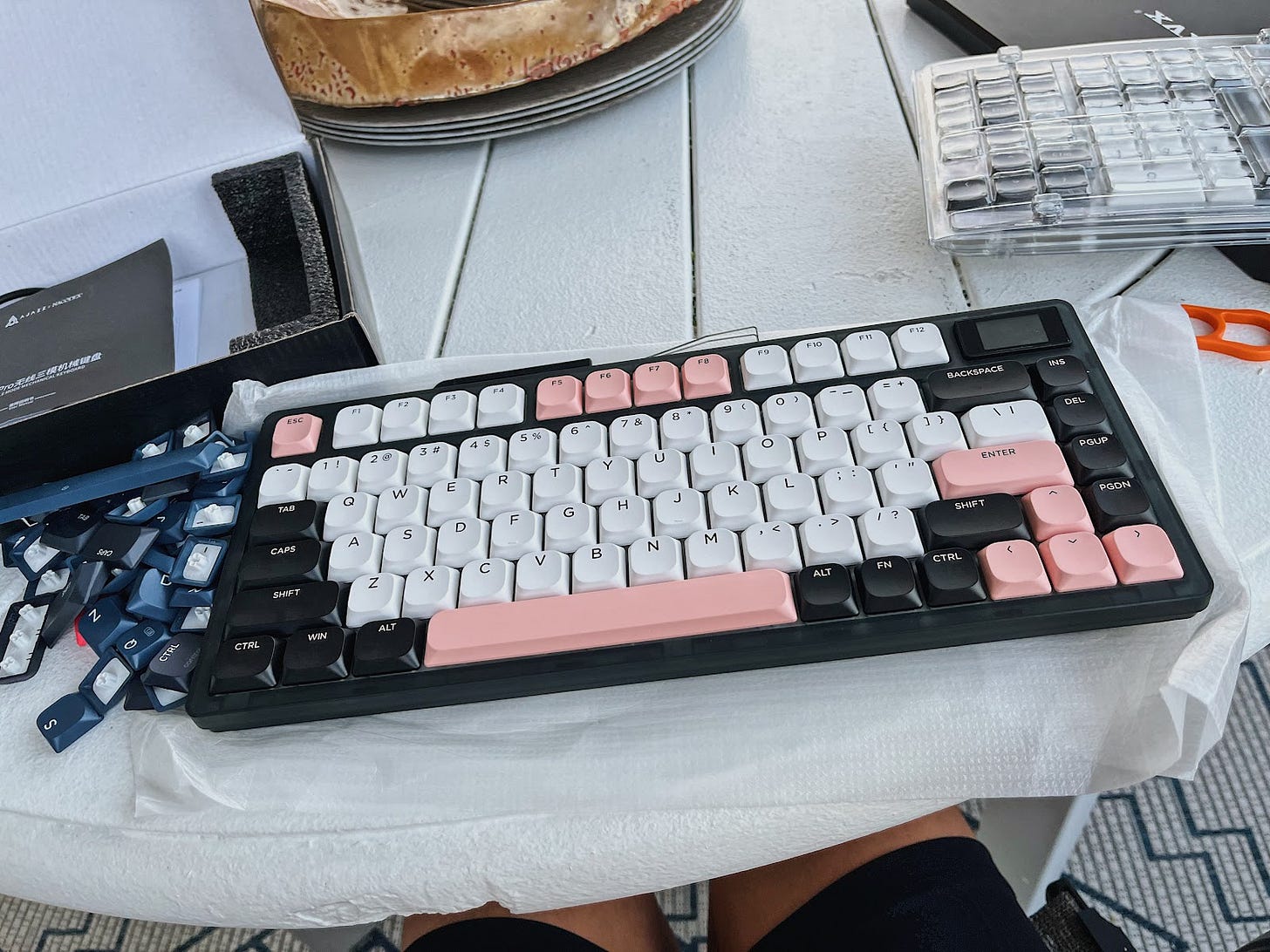 Black, pink, and white mechanical keyboard on a white table at an areal view.