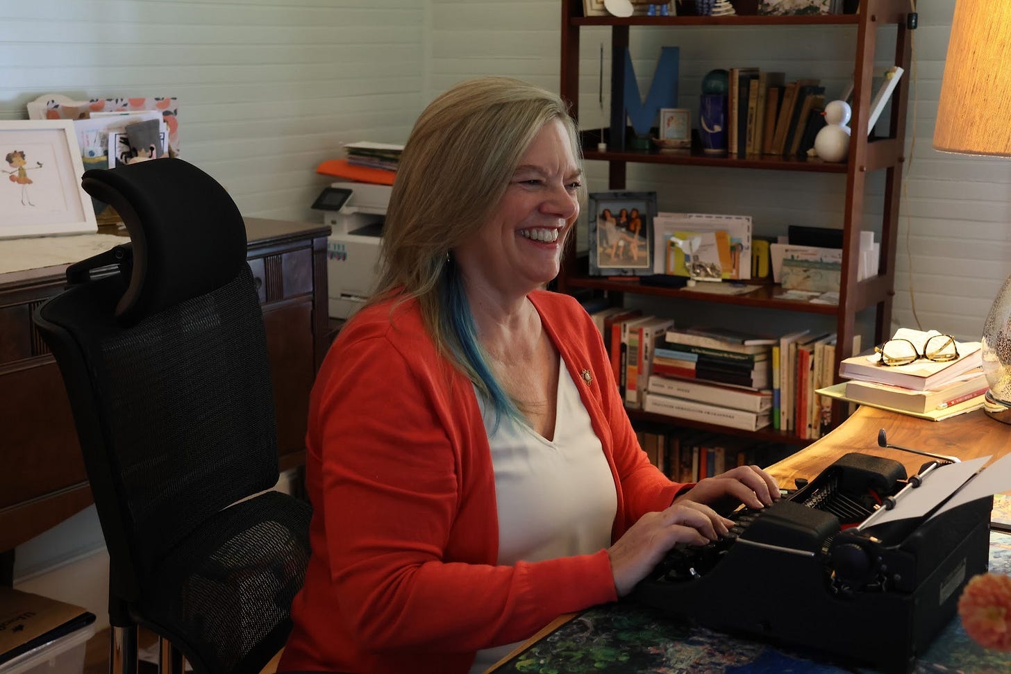 Melora Fern sitting at a black typewriter at her desk. She is smiling big