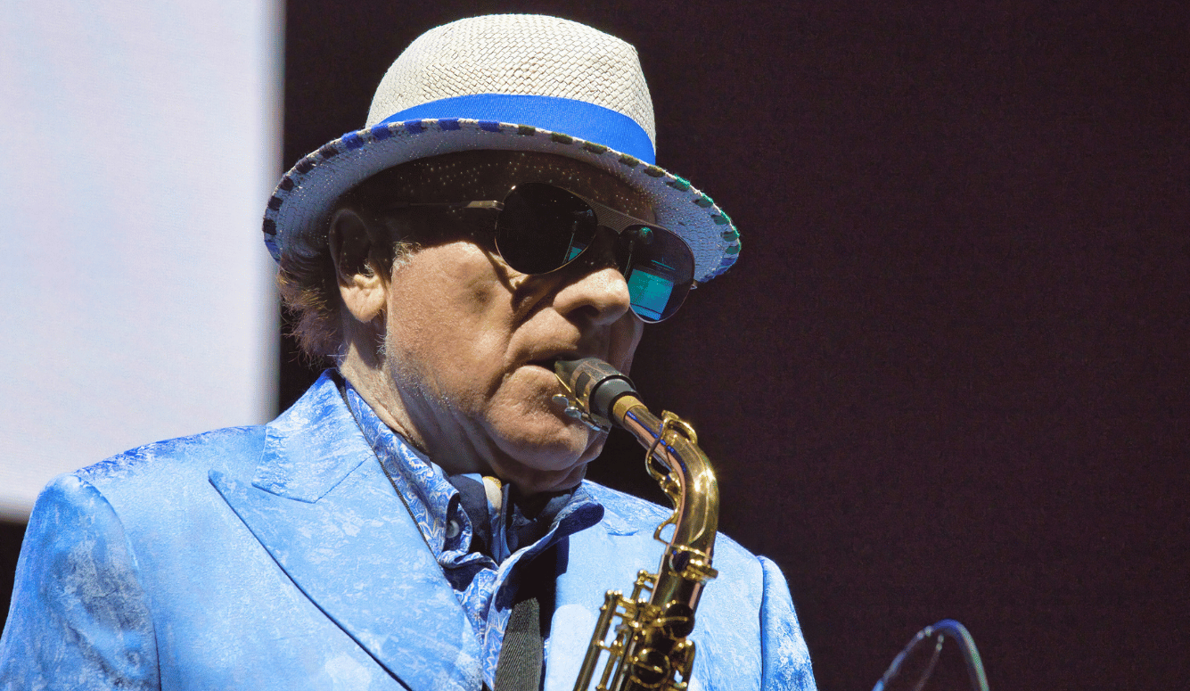 Van Morrison lays saxophone on stage. He wears a hat and polarised aviator sunglasses. Van Morrison lays saxophone on stage. He wears a hat and polarised aviator sunglasses.