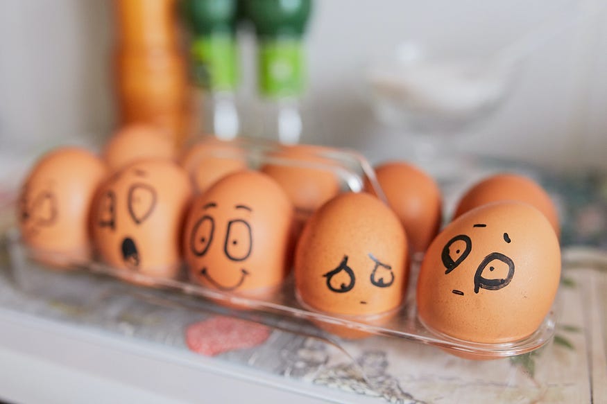 a tray of eggs, with different faces drawn onto them,from smiley to sad.