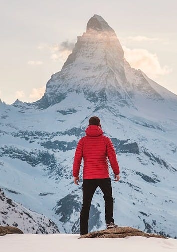 person in red hoodie standing on snowy mountain during daytime person in red hoodie standing on snowy mountain during daytime