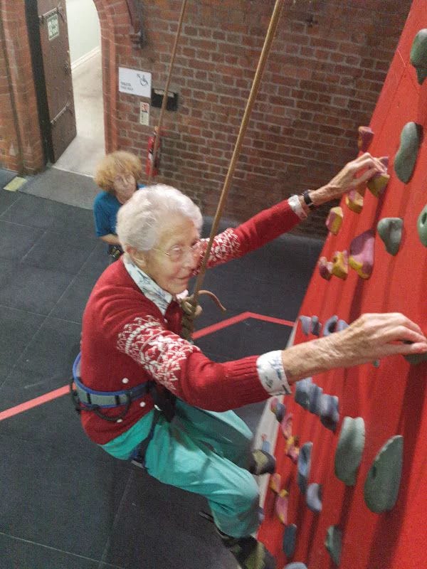 This may contain: an older woman climbing up the side of a wall