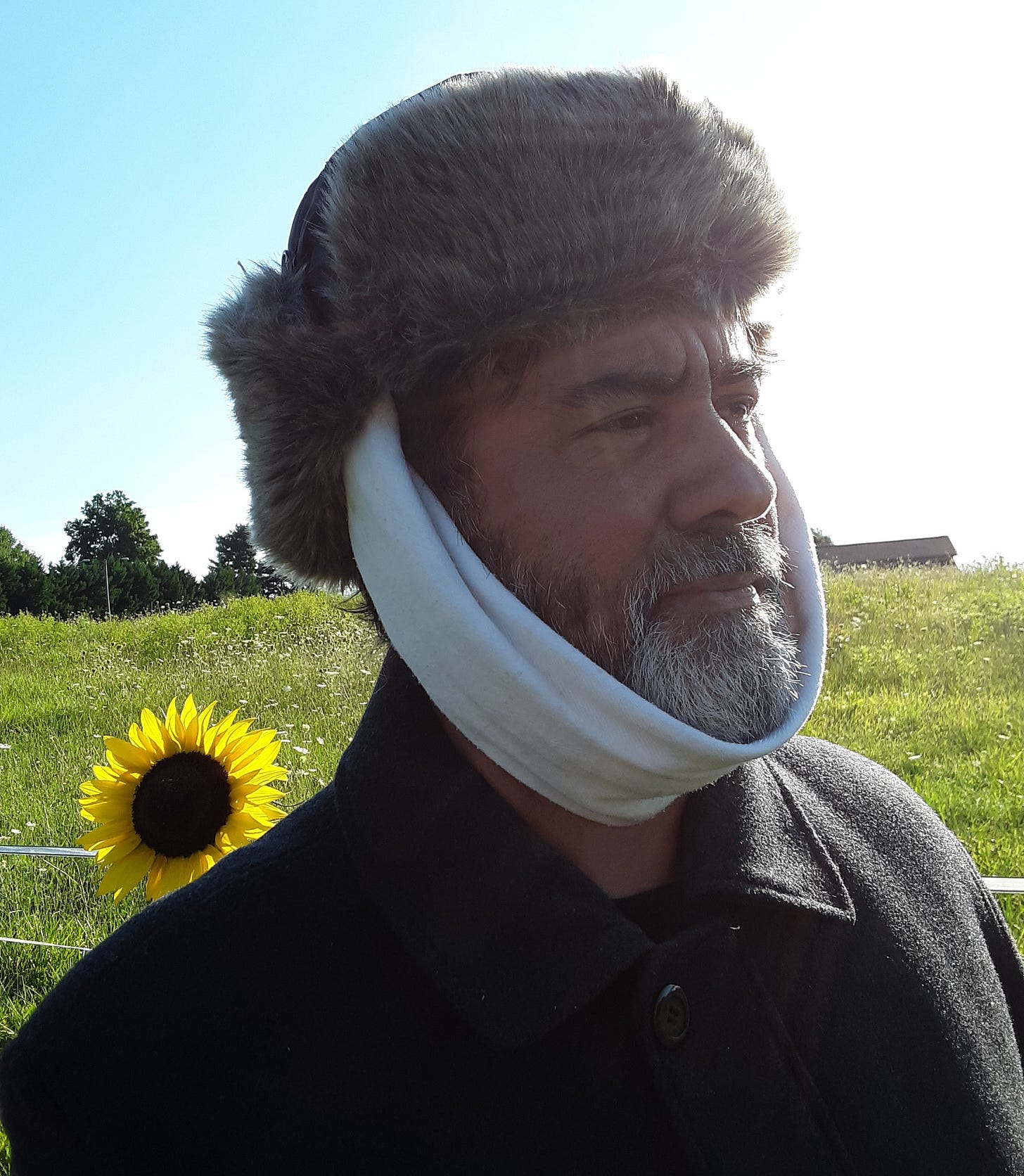 Ernesto cosplaying at Vincent Van Gogh in his painting "Self-portrait with Bandaged Ear." He wears a fur-trimmed hat, heavy coat, and a white bandage. A sunflower appears behind his right shoulder, and there is a great deal of glare from the bright sun.