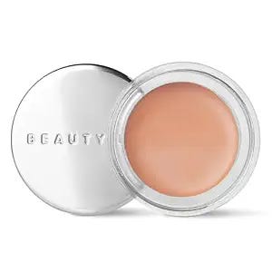 A compact jar of Beauty Pie Superluminous Under Eye Genius Corrector, revealing a smooth, peach-toned cream used for color-correcting and brightening the eyelids. A compact jar of Beauty Pie Superluminous Under Eye Genius Corrector, revealing a smooth, peach-toned cream used for color-correcting and brightening the eyelids.