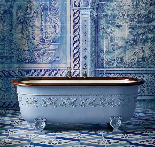 Ornate bathroom interior with walls and floor covered in blue and white azulejo tiles featuring detailed patterns of landscapes architectural elements and foliage a central clawfoot bathtub painted in soft blue with intricate carved floral and scrollwork designs on its sides and brass faucets mounted on the edge the tub stands on four decorative claw feet the overall scene evokes Portuguese tile artistry with vibrant blue tones dominating the composition Ornate bathroom interior with walls and floor covered in blue and white azulejo tiles featuring detailed patterns of landscapes architectural elements and foliage a central clawfoot bathtub painted in soft blue with intricate carved floral and scrollwork designs on its sides and brass faucets mounted on the edge the tub stands on four decorative claw feet the overall scene evokes Portuguese tile artistry with vibrant blue tones dominating the composition