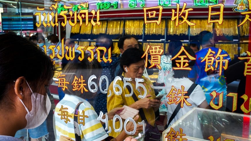 People crowd into a gold shop with Chinese writing on the window with numbers