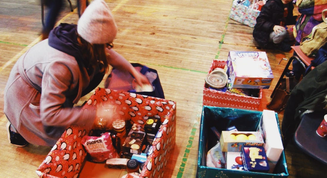 A woman packing a wrapped box with grocery items from a blue bag, sitting on a wooden floor A woman packing a wrapped box with grocery items from a blue bag, sitting on a wooden floor