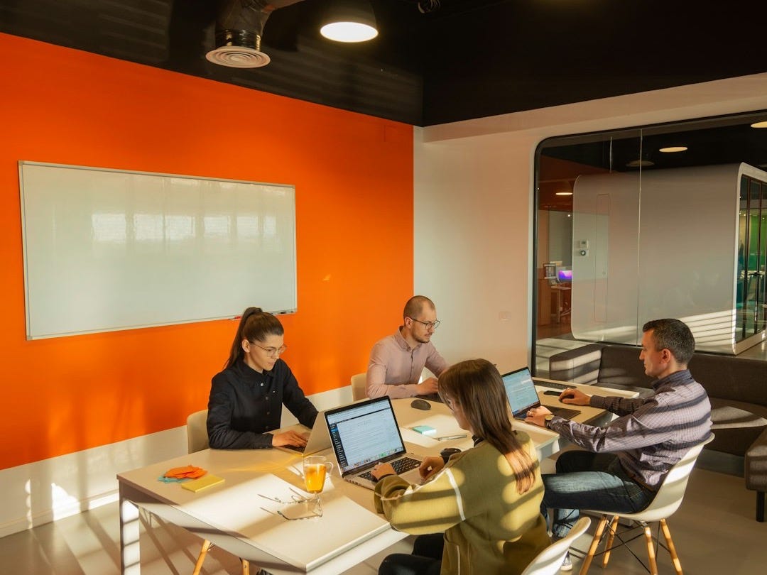 a group of people sitting around a table with laptops a group of people sitting around a table with laptops