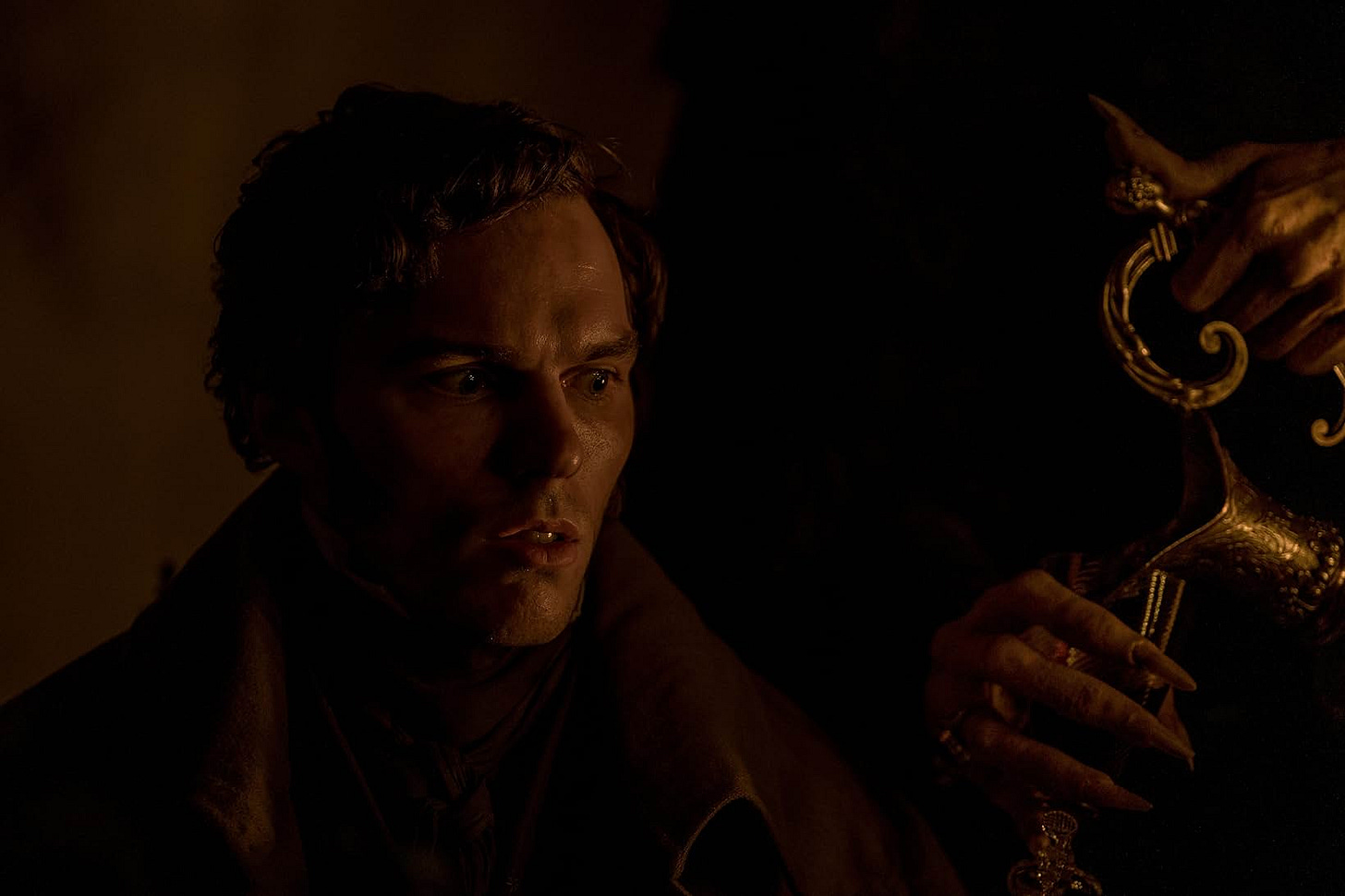 A still from the film. Nicholas Hoult watches, terrified, as a hand pours wine into his goblet.