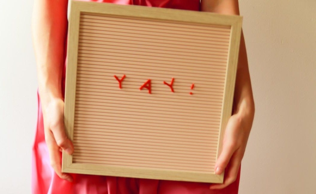 Person holds a sign saying "yay!" excitedly.