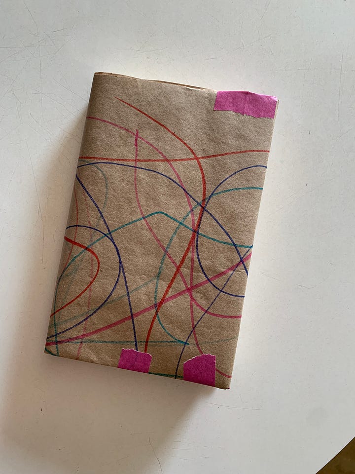first image: a book covered in brown paper, covered in colorful stripes, on a white background, two: a blue painted book on a white background, the top of a black cat's head is visible