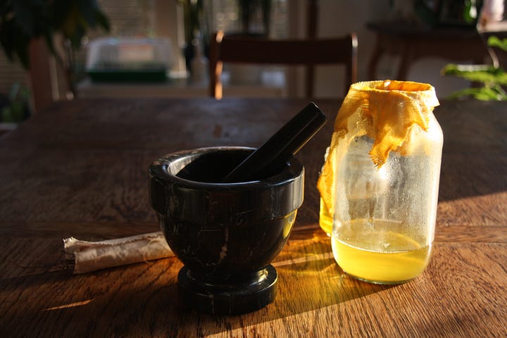 Jars of brightly coloured liquids in the process of making pigments. The yellow is bright in the morning sunlight. The pigment is heavy at the bottom of the jars with a gradient of colour.