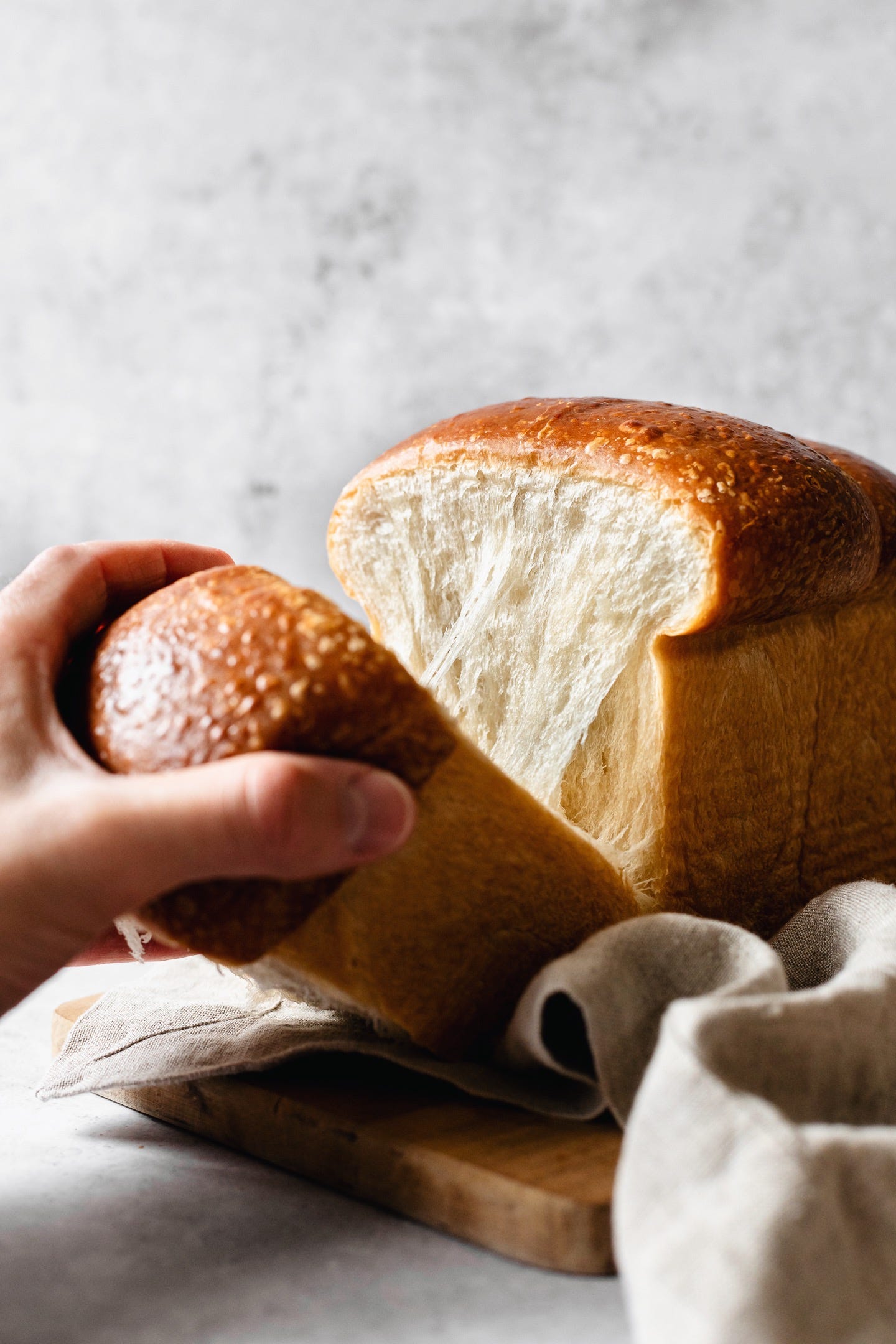 Hand tearing piece of vegan milk bread loaf on grey background