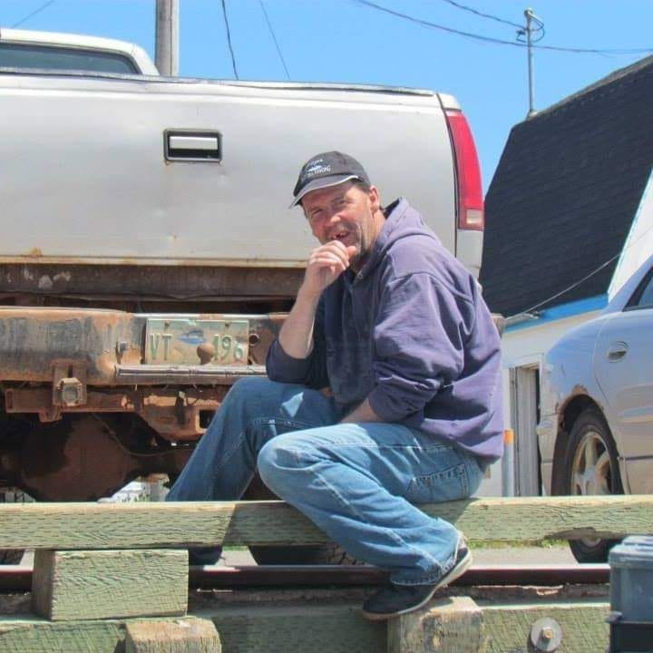 Right: man standing on a fishing boat on the water. Right: man sitting a harbour ledge behind a vehicle. 