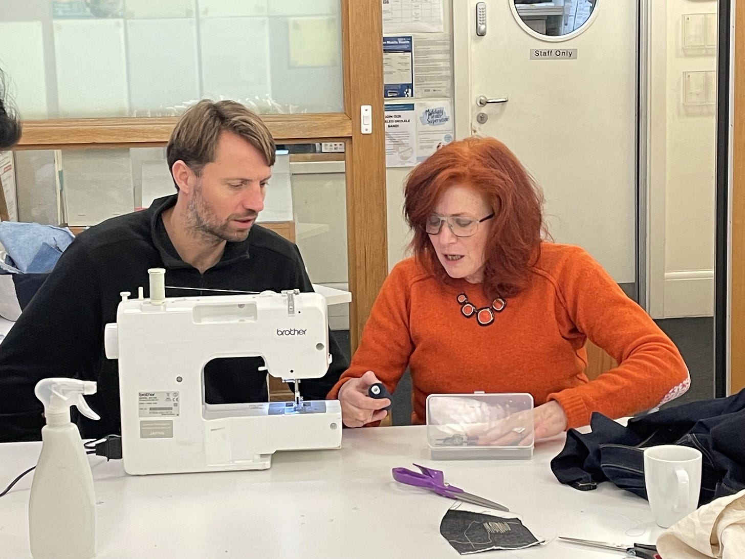A man and a woman sitting at a sewing machine.