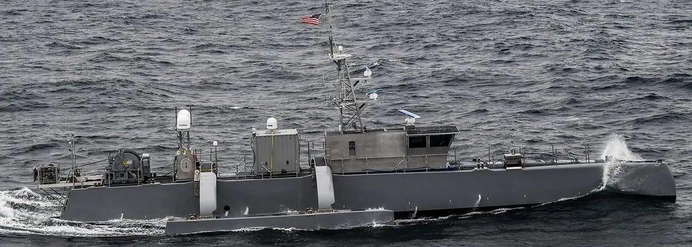 The image shows two U.S. Navy vessels operating together at sea. In the foreground is a smaller unmanned surface vessel (USV) displaying an American flag, while in the background is a larger Arleigh Burke-class guided-missile destroyer. The vessels appear to be conducting joint maritime operations in open ocean conditions. The image shows two U.S. Navy vessels operating together at sea. In the foreground is a smaller unmanned surface vessel (USV) displaying an American flag, while in the background is a larger Arleigh Burke-class guided-missile destroyer. The vessels appear to be conducting joint maritime operations in open ocean conditions.