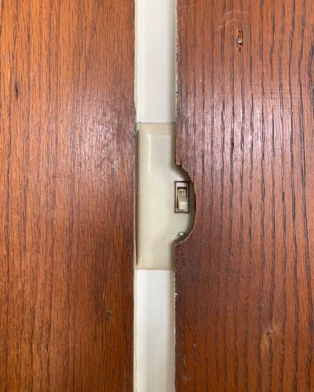 light switch covered by a wood panel that's cut out to allow the switch part to be turned on and off