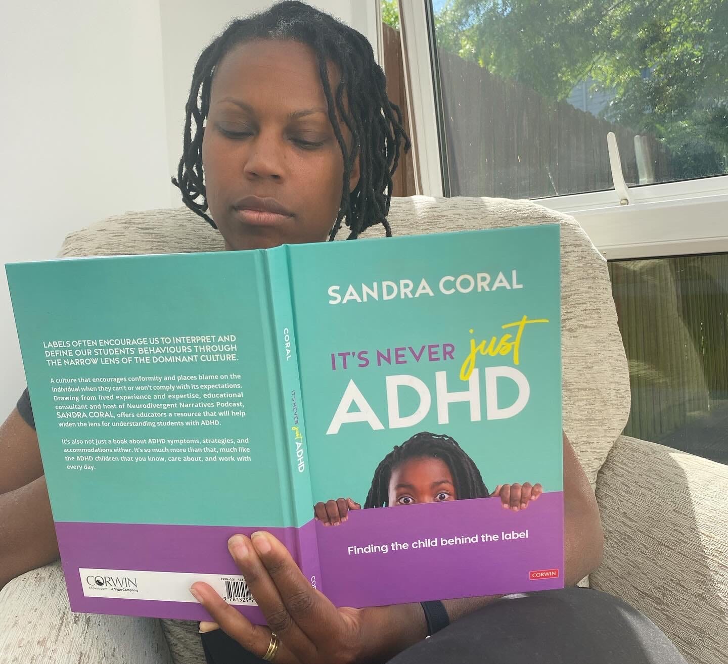 Sandra is a Black femme with short black locs reading their book It's Never Just ADHD