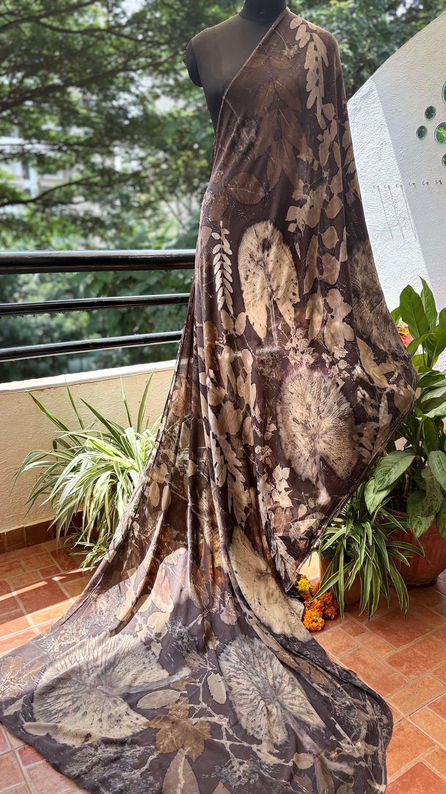 Mannequin draped in a dark eco-printed textile with large botanical leaf silhouettes.