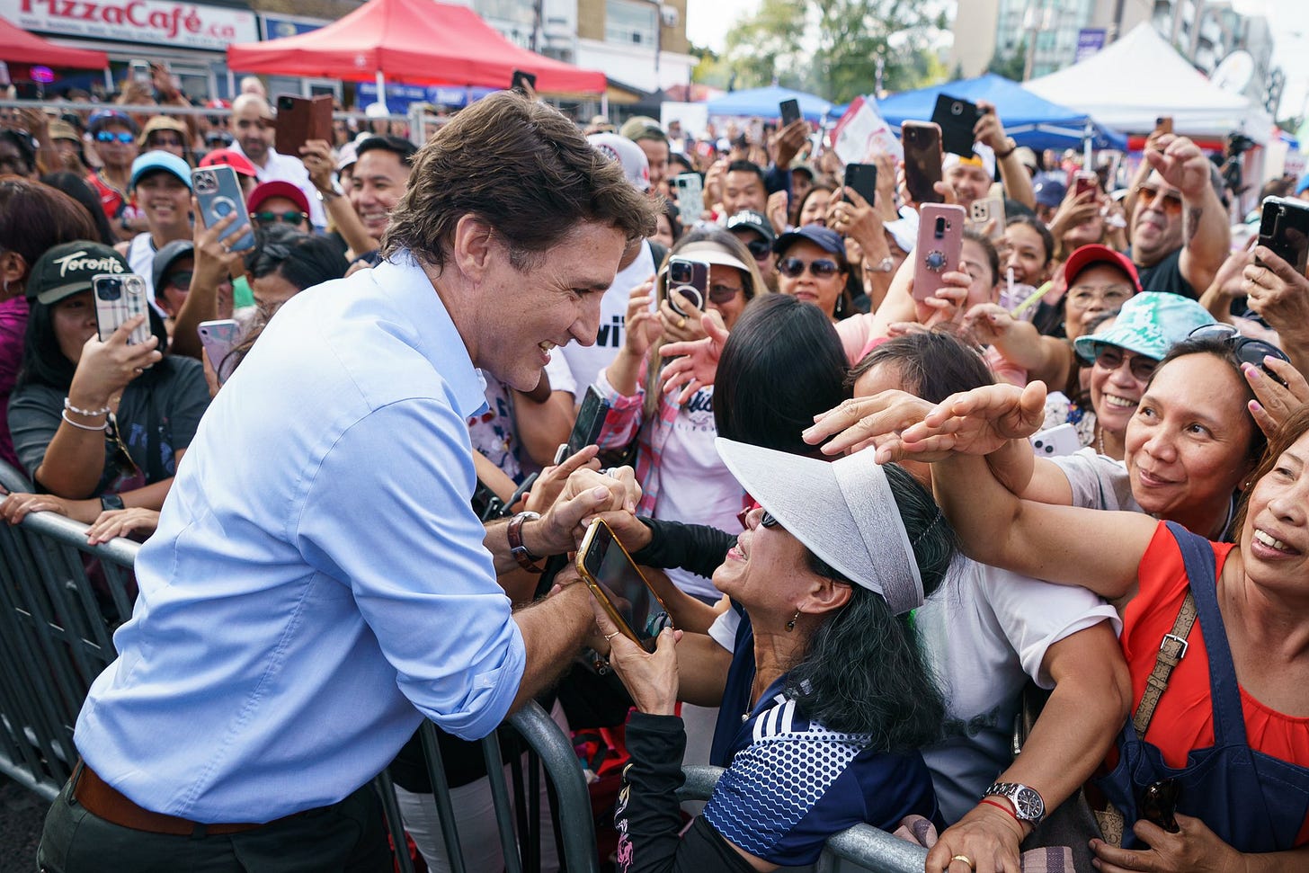 Prime Minister Justin Trudeau is shaking hands with a person. A large crowd of people is standing in front of him and beside him. Prime Minister Justin Trudeau is shaking hands with a person. A large crowd of people is standing in front of him and beside him.