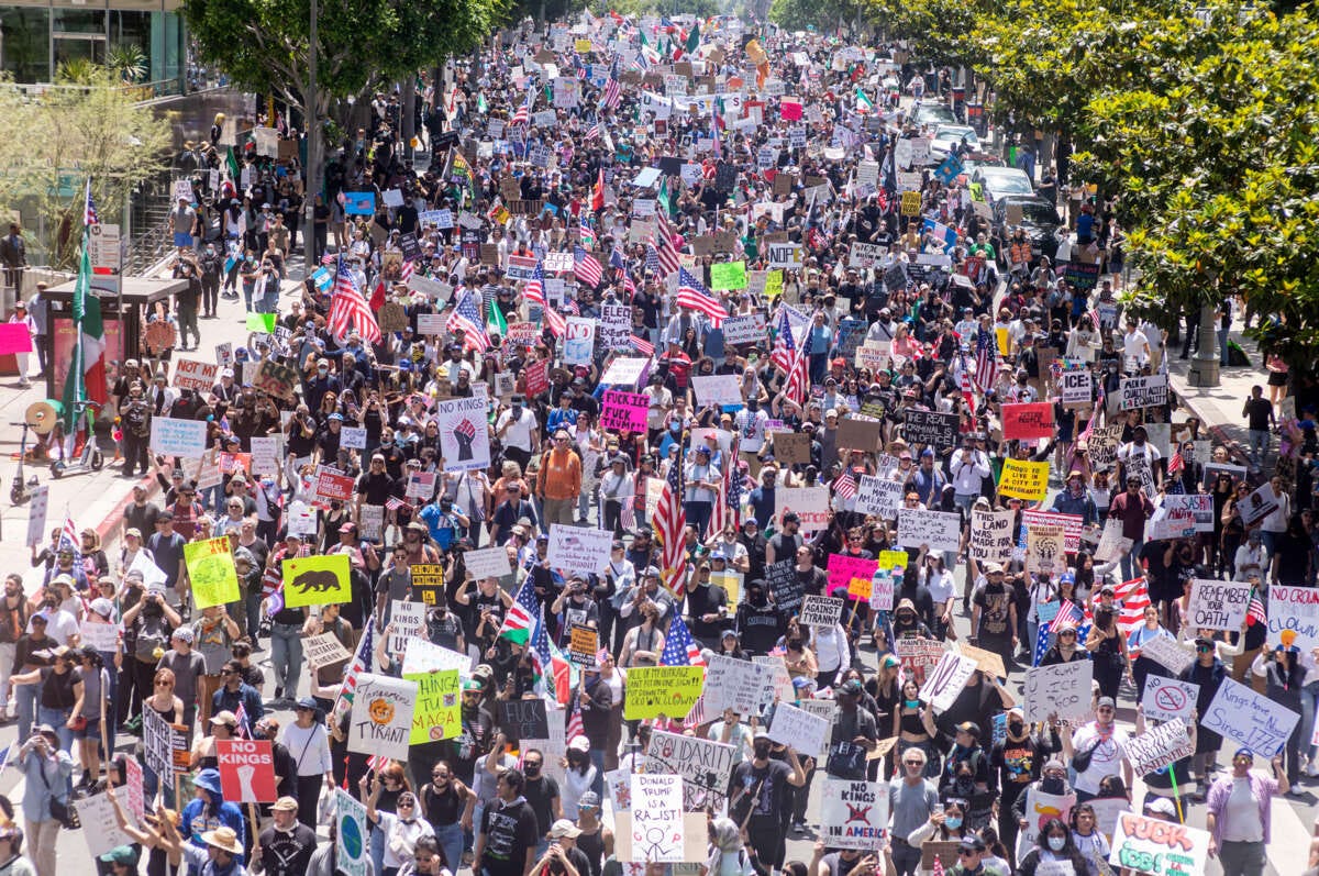 People waving flags and carrying signs fill a street during the No Kings protest