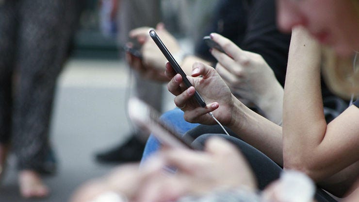 a line of people sitting, scrolling on their phones
