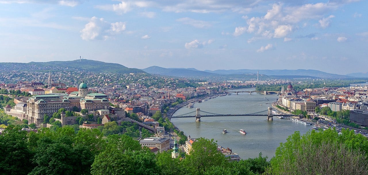 Panoramic view of Budapest from Gellért Hill, with the Danube cutting through the city and major landmarks stretching across the skyline under clear daylight. Panoramic view of Budapest from Gellért Hill, with the Danube cutting through the city and major landmarks stretching across the skyline under clear daylight.