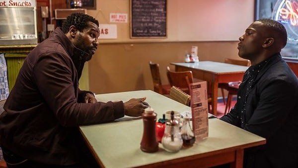 This image shows Aaron Sinclair (played by Daniel Adegboyega, left) sitting at a diner table across from his son, Ryan Sinclair (played by Tosin Cole, right). Ryan leans his head back, looking skeptically at his father, who taps his right hand on the tabletop to emphasize a point he's making. This image shows Aaron Sinclair (played by Daniel Adegboyega, left) sitting at a diner table across from his son, Ryan Sinclair (played by Tosin Cole, right). Ryan leans his head back, looking skeptically at his father, who taps his right hand on the tabletop to emphasize a point he's making.